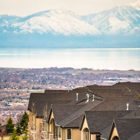 Square frame Luxurious homes with valley lake mountain and cloudy sky in the background. The houses have porches, semi-circle balconies, and conifers growing on the snowy yards.の写真素材