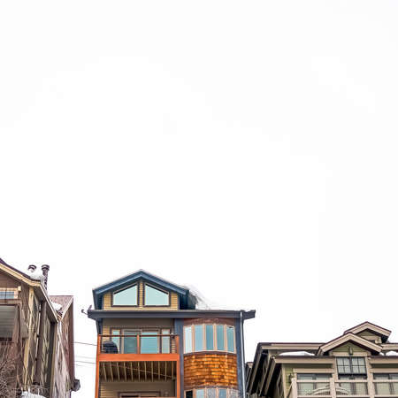 Square frame Exterior view of houses with balconies and built on a hill against cloudy sky. The slope is covered with fresh white snow during winter season.の写真素材