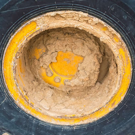 Square frame Close up view of the heavy duty black rubber tire of a construction vehicle. Caked mud can be seen on the yellow wheel rim and body of the machinery.の写真素材