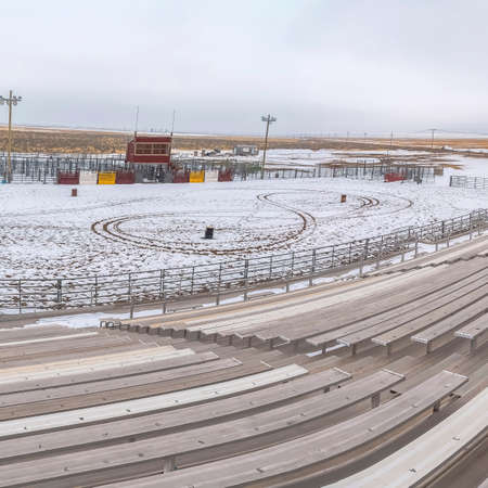 Square frame Bleachers overlooking a sports field covered with snow in winter. Vast terrain and cloud filled sky can also be viewed from the tiered seats.の写真素材