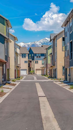 Vertical frame Road in the middle of homes with view of snow capped mountain and cloudy sky. The houses have white garage doors and small balconies.の写真素材