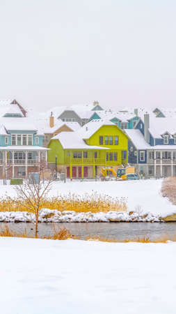 Vertical frame Houses overlooking a calm lake with bridge on a cloudy winter day. The roof of the homes as well as the ground are covered with fresh white snow.の写真素材