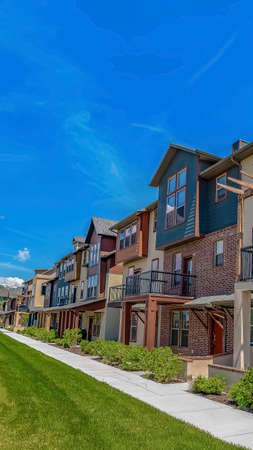 Vertical Row of homes with porches and small balconies under blue sky on a sunny day. A paved pathway and grassy terrain can be seen in front of the residences.の写真素材