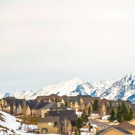 Square Homes along a paved mountain road against bright cloudy sky in winter. The residential area has a magnificent view of a towering snow peaked mountain.の写真素材