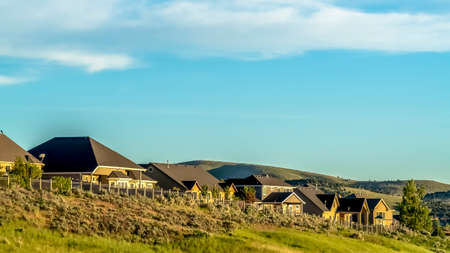 Panorama Residences on a hill with peaceful blue sky and clouds overhead on a sunny day. The homes has dark roofs and beige exetrior walls.の写真素材