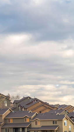 Vertical Rows of houses built on a mountain slope with view of cloudy sky overhead. A bit of powdery snow can be seen near top of the mountain.の写真素材