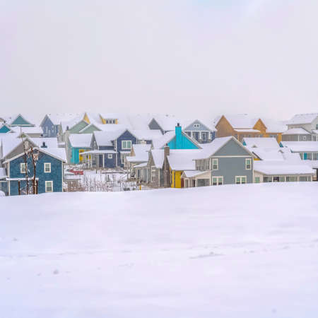 Square frame Winter landscape with colorful houses against a cloudy sky background. A vast terrain blanketed with fresh snow can be seen in the foreground.の写真素材