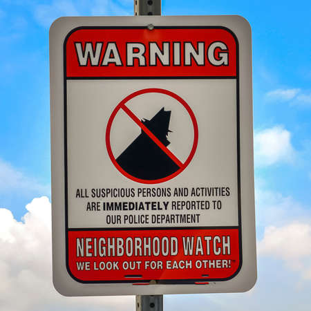 Square frame Close up of a Warning sign on a neighborhood against cloudy blue sky background. The sign gives a warning that suspicious persons and activities are reported to the Police Department.の写真素材