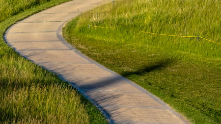Panorama frame Pathway that winds through a grassy terrain with houses in the background. The landscape is illuminated by sunlight on this sunny day.の写真素材