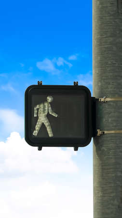 Vertical Close up of pedestrian traffic light signal against blue sky and bright clouds. The...