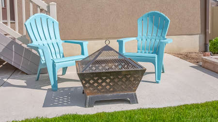 Panorama Square fire pit and blue plastic chairs on the yard of a home on a sunny dayの写真素材