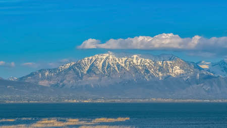 Panorama Vivid blue sky with puffy clouds over a snow peaked mountain and calm lakeの写真素材