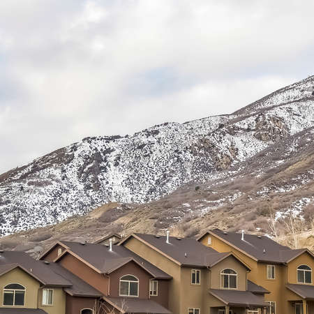 Square frame Homes against a snow covered mountain top and blue sky filled with thick clouds