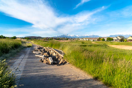 Damaged road with a huge hole amid grassy terrain and houses on a sunny dayの写真素材