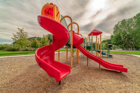 Playground with bright red slides against trees and cloudy sky backgroundの写真素材