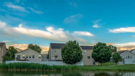 Panorama frame Pathway along a shiny pond on a grassy terrain with homes in the background
