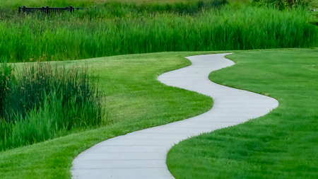 Panorama frame Pathway and pond on grassy terrain with homes lake and mountain backgroundの写真素材
