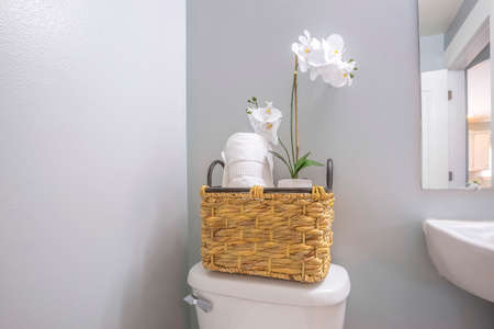Woven basket with tissue roll and white flowers placed on top of the toilet tank
