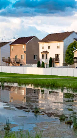 Vertical frame Homes and cloudy sky reflected on the shiny surface of a grassy pond. Narrow pathways can also be seen amid the grass covered landscape.の写真素材