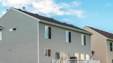 Panorama A house with gray horizontal wood siding and stairs that leads to the balcony. The house alos has sliding windows and door and dark roof.の写真素材