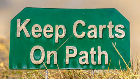 Panorama frame Close up view of a green and white sign that reads Keep Carts On Path. The signage is...