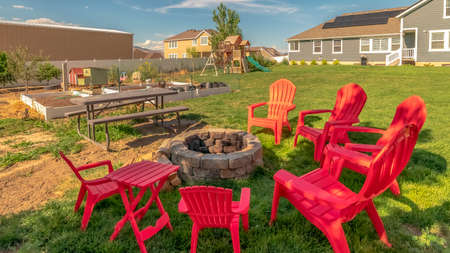 Panorama Backyard chairs around a stone fire pit adjacent to a picnic table with bench. Planting...