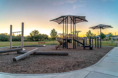 Neighborhood park viewed at sunset with trees homes and blue sky background. The children's...