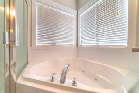 Close up of a gleaming white bathtub adjacent to the shower stall and windows