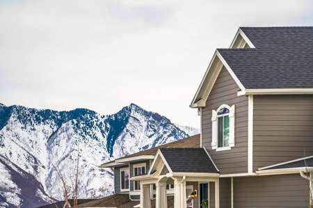 Home with gray exterior wall and stricking view of snowy mountain in winter. The residence have an arched window with shutters, and front porch with pillars.の写真素材