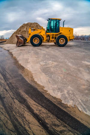 Yellow bulldozer on a road with mound of soil and cloudy sky background. The construction vehicle...