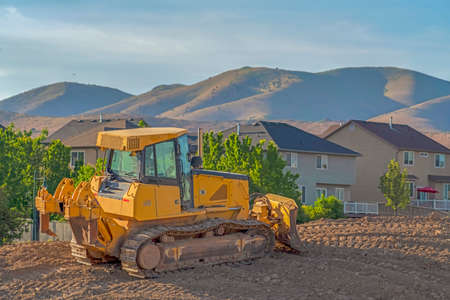 Construction sitewith yellow bulldozer against homes and mountain on a sunny day. The vehicle has...