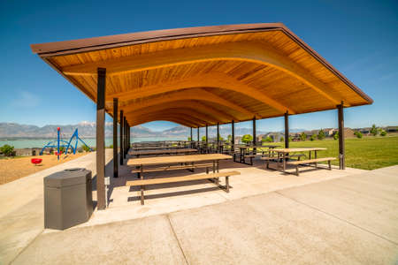 Pavilion at a park with view of lake and Timpanogos mountains on a sunny day. Children's playground and houses can also be seen around the picnic area.