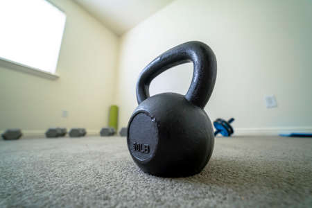 Close up of black kettlebell inside a gym room with carpet floor and white wall. The weight of the heavy equipment is embossed on its surface.の写真素材