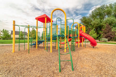 Colorful playground equipment with tube slide bridge climbing bars and stairs. Building, trees, and...