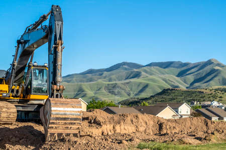 Front view of a yellow excavator at a construction site against mountain and sky. The machinery has...