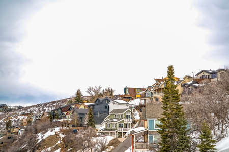 Houses on a mountain slope with snow and conifers during winter in Park City. A bright sky filled...