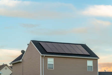 Exterior view of a home with solar panels on the roof under blue sky and clouds. The house features gray wall, dark roof, and small windows.の写真素材