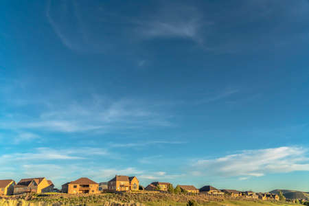 Blue sky and clouds over houses and grass covered hill viewed on a sunny dayの写真素材