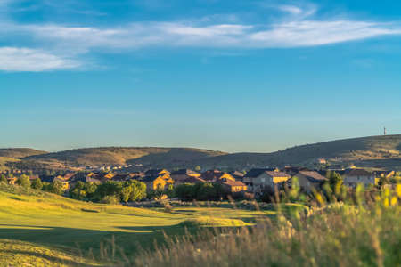 Neighborhood homes around a sunlit golf course with distant mountain backgroundの写真素材
