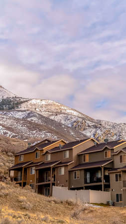 Vertical frame Cluster housing development on a mountain slope below a snow covered peak in spring in a high altitude rural landscapeの写真素材