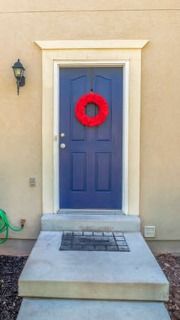 Vertical Concrete steps leading to the blue wooden front door of a home with a red wreath. Bright green plants grow on the yard of this residence.の写真素材