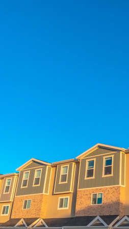 Vertical frame Facade of townhouses illuminated by sunlight with vibrant blue sky background. The homes have sliding windows and combination of brick, concrete, and wood wall.の写真素材
