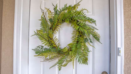 Panorama Close up of a simple fern wreath hanging on the white wood front door of a home. A doorbell can also be seen at this house entrance.の写真素材