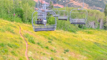 Panorama Chairlifts over mountain with grasses and trails in Park City Utah in summer. The people on the ski lifts has an amazing aerial view of the ski resort during off season.の写真素材