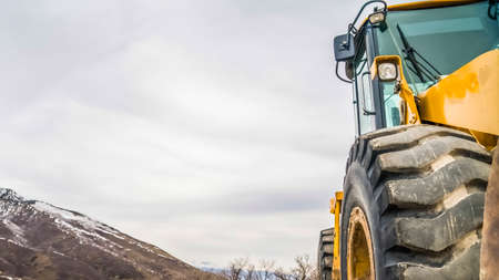 Panorama Close up of the tires of a bulldozer against snow peaked mountain and cloudy skyの写真素材