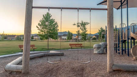 Panorama Childrens playground at a park with swings slides and umbrellas viewed at sunset