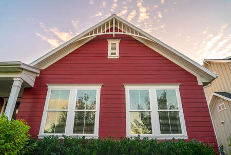 Colorful red timber clad house in day. Colorful red timber clad house with white windows viewed low angle over a green hedge against a blue skyの写真素材