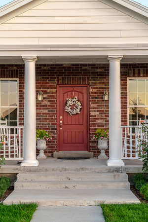 Front door to a house flanked by two pillars. Front door to a face brick house flanked by two pillars and windows with a dried wreath hanging on the woodの写真素材