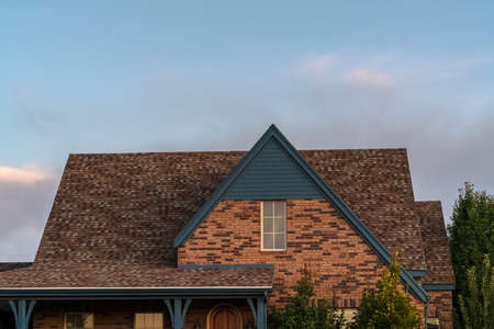 House with steeply pitched roof near sunset. House with steeply pitched roof and attic window in a face brick facade against a cloudy evening skyの写真素材