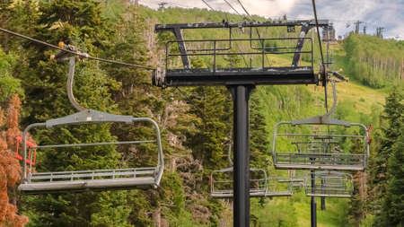 Panorama frame Chairlifts against vivid green trees and cloudy sky at Park City in off season. The ski resort mountain landscape with hiking trails viewed in summer.の写真素材